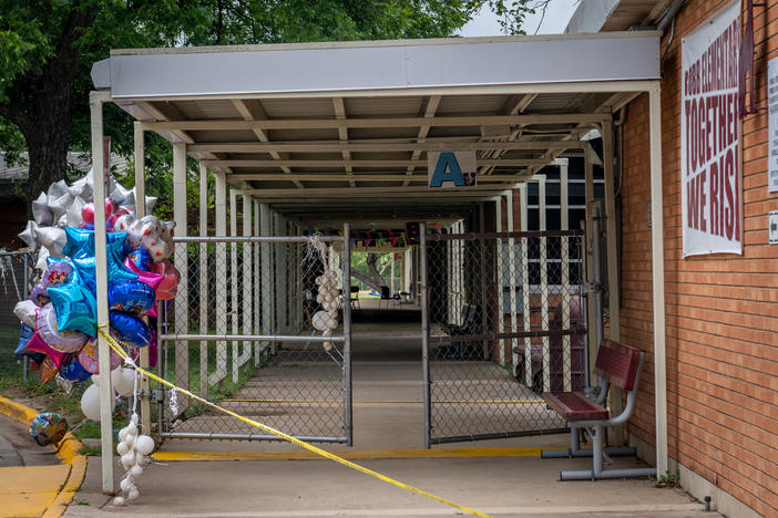 Balloons and caution tape are seen at the entrance to Robb Elementary School in Uvalde, Texas, on Tuesday. Investigators had initially said a teacher left a back door propped open at the school, but that account has now shifted.