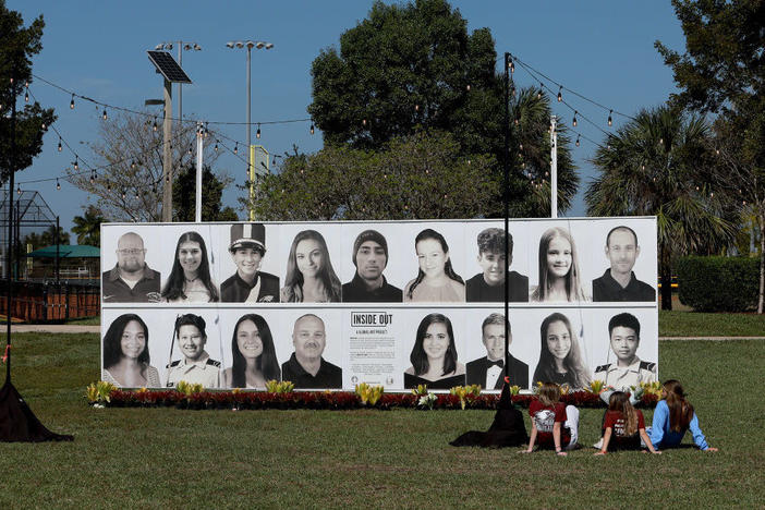 People sit Feb. 14 in front of a photo display of the 17 people killed four years earlier during a mass shooting at Marjory Stoneman Douglas High School in Parkland, Fla.