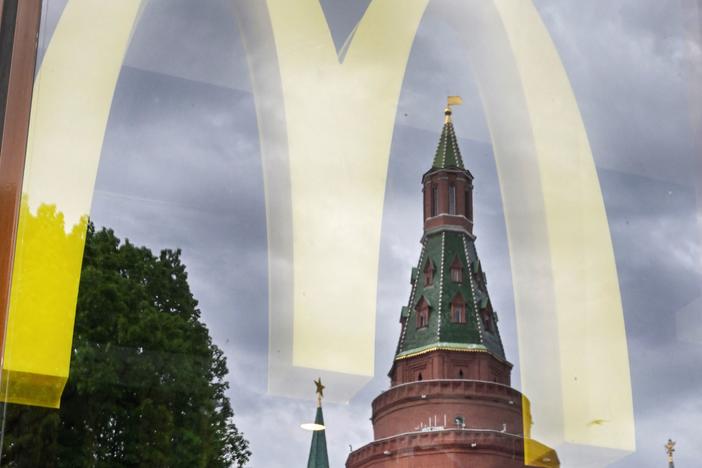 People walk past a window of a McDonald's restaurant as the towers of the Kremlin reflect in it in Moscow on May 26, 2022.