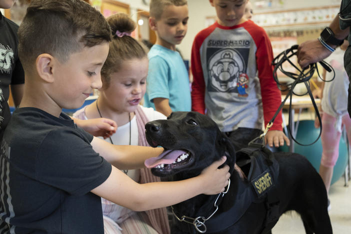Freetown Elementary School students Mason Santos, left, and Mila Talbot, right, pet Hunter the dog after she finishes checking a classroom.
