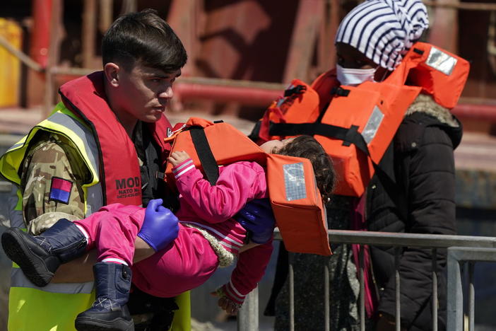 A soldier carries a child from a group of people thought to be migrants are brought in to Dover, England, by Border Force, following a small boat incident in the Channel, Tuesday June 14, 2022.