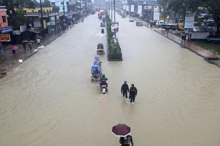 People wade through flooded waters in Sylhet, Bangladesh, Saturday, June 18, 2022. At least 18 people have died as floods cut a swatch across northeastern India and Bangladesh, leaving millions of homes underwater.