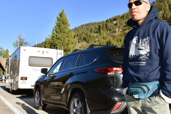Muris Demirovic waits by his rental car outside Yellowstone National Park for the entrance gate to open on Wednesday morning, near Wapiti, Wyo.