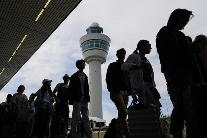 Travelers wait in long lines outside the terminal building to check in and board flights at Amsterdam's Schiphol Airport, Netherlands, Tuesday, June 21, 2022.
