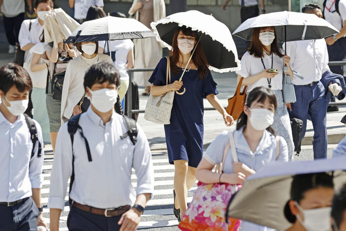 People, some of them holding parasols, cross an intersection amid heat, in Tokyo, Monday, June 27, 2022.