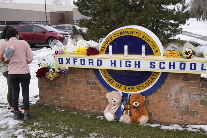 Students stand outside Oxford High School, near memorial items that were placed after the November 2021 shooting that took place at the Michigan school.