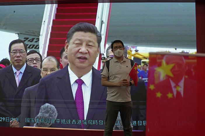 A visitor poses for a photograph in front of a TV showing Chinese president Xi Jinping at an exhibition to mark the 25th anniversary of the former British colony's return to Chinese rule, in Hong Kong, Friday, June 24, 2022.