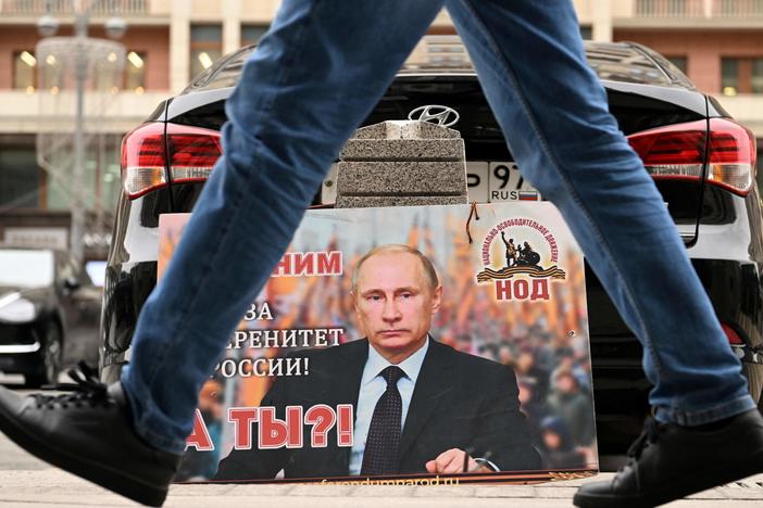 A placard featuring an image of Russian President Vladimir Putin and reading "We are with him for the sovereignty of Russia! And you?" is seen left in front of the Russian State Duma building in central Moscow on February 24, 2022.
