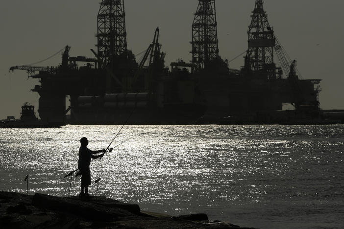 A man wears a face mark as he fishes near docked oil drilling platforms, Friday, May 8, 2020, in Port Aransas, Texas.