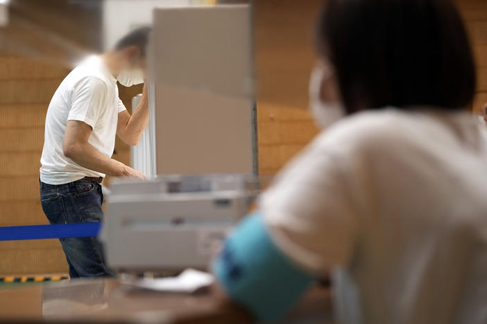 A staff member of a local election administration watches a voter preparing his ballot in the upper house elections at a polling station Sunday, July 10, 2022, in Tokyo.