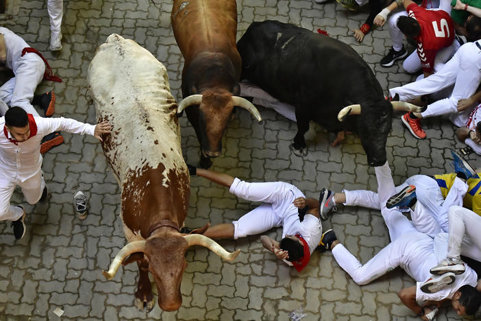 Runners fall during the running of the bulls at the San Fermin Festival in Pamplona, northern Spain, Monday, July 11, 2022.