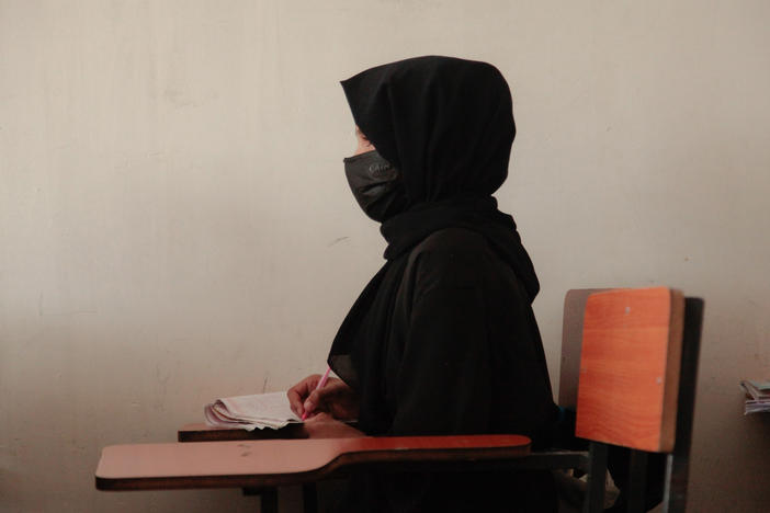 A teenage girl wearing a face mask, head scarf and long black robe listens to a math teacher at a tutoring center in Kabul. The center was established by a women's rights activist to circumvent a Taliban ban on girls attending secondary school. The activist said she has informal permission by Taliban authorities to run the center as long as teenage girls abide by a strict dress code.