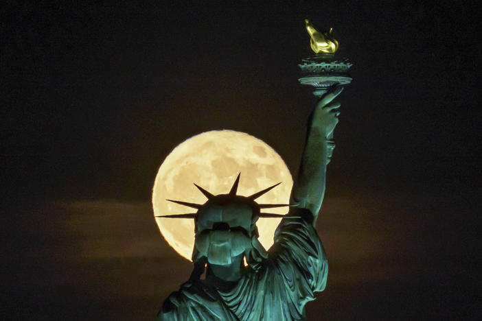 The strawberry supermoon rises in front of the Statue of Liberty in New York on June 14. After July's supermoon on Tuesday there will be one more for the year on Aug. 11.