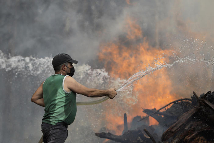 A local resident uses a garden hose to try to stop a forest fire from reaching houses in the village of Figueiras, outside Leiria, central Portugal, Tuesday, July 12, 2022.