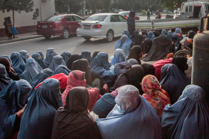 Women in burkas sit outside a bakery in Kabul. Impoverished women from hilltop slums around Kabul have been flocking to bakeries in the city, silently waiting to see if someone will purchase bread for them.