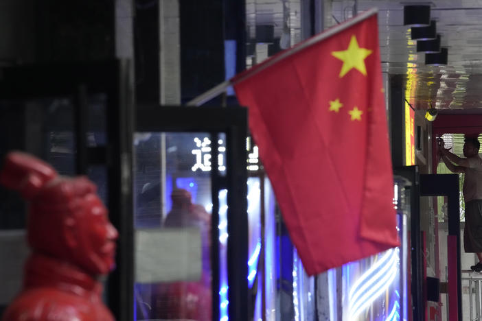 A worker stands on a platform near a Chinese national flag, Friday, July 15, 2022, in Beijing. China's economy contracted in the three months ending in June compared with the previous quarter after Shanghai and other cities shut down to fight coronavirus outbreaks, but the government said a "stable recovery" is under way after businesses reopened.