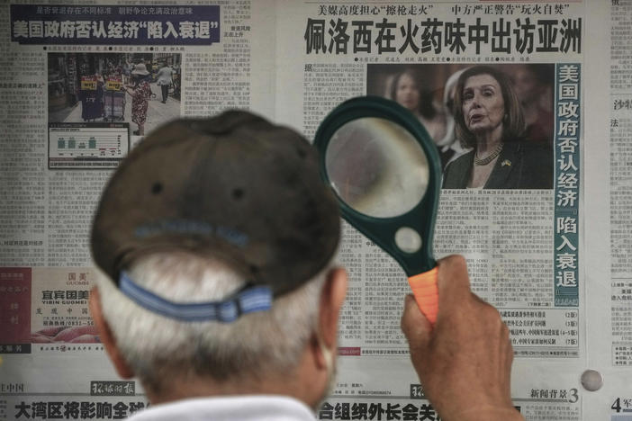 A man uses a magnifying glass to read a newspaper headline reporting on U.S. House Speaker Nancy Pelosi's Asia visit, at a stand in Beijing, Sunday, July 31, 2022.
