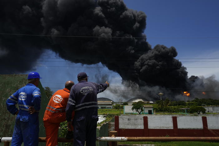 Workers of the Cuba Oil Union, known by the Spanish acronym CUPET, watch a huge rising plume of smoke from the Matanzas Supertanker Base, as firefighters work to quell a blaze which began during a thunderstorm the night before, in Matazanas, Cuba, Saturday, Aug. 6, 2022.
