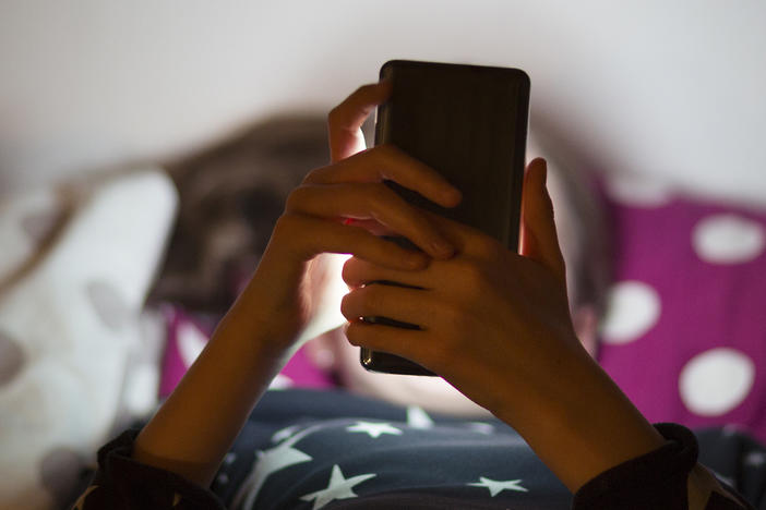 Snapchat is rolling out new parental controls that allow parents to see their teenager's contacts and confidentially report to the social media company any accounts that concern them. A child lies in bed illuminated by the glow of a cell phone.