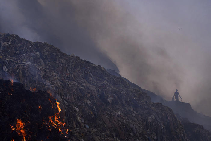 A person picks through trash for reusable items as a fire rages at the Bhalswa landfill in New Delhi, April 27, 2022.