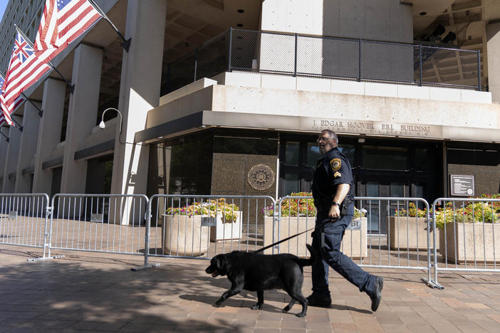 A Federal Bureau of Investigation police officer walks with his working dog outside Federal Bureau of Investigation building headquarters in Washington, Saturday, Aug. 13, 2022.
