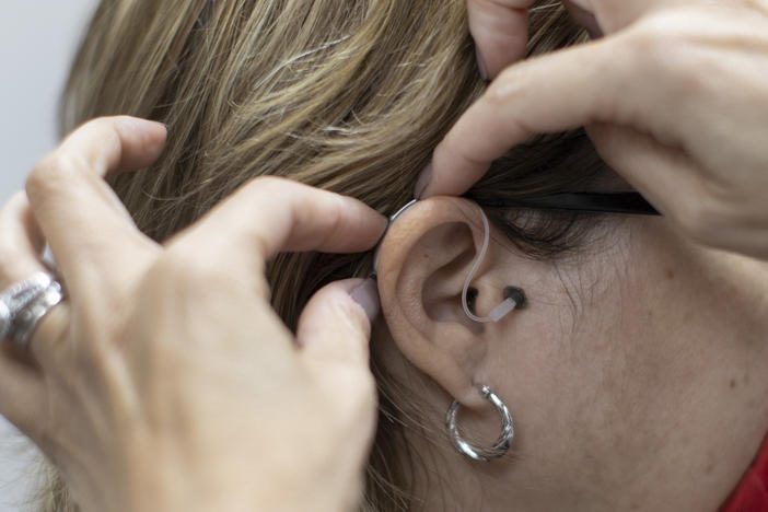 In this photo illustration, Janine Ramirez, a hearing aid specialist with Hear Again America, places a hearing aid on an ear Oct. 20, 2021, in Fort Lauderdale, Fla.