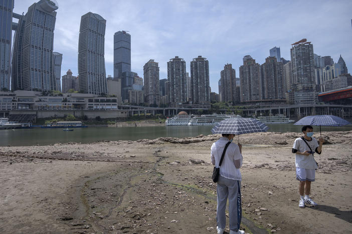 Students carrying umbrellas stand on the dry riverbed of the Jialing River in southwestern China's Chongqing Municipality, Friday, Aug. 19, 2022.