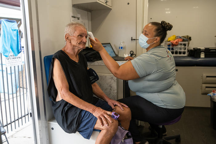 Alicia Williams checks the vital signs of Paul Yager inside the mobile medical unit parked outside St. Vincent de Paul, a charitable organization with a soup kitchen in Phoenix's Sunnyslope neighborhood, on Aug. 9. Yager, 64, is unsheltered, lives with preexisting conditions and has been waiting for housing assistance for two years.