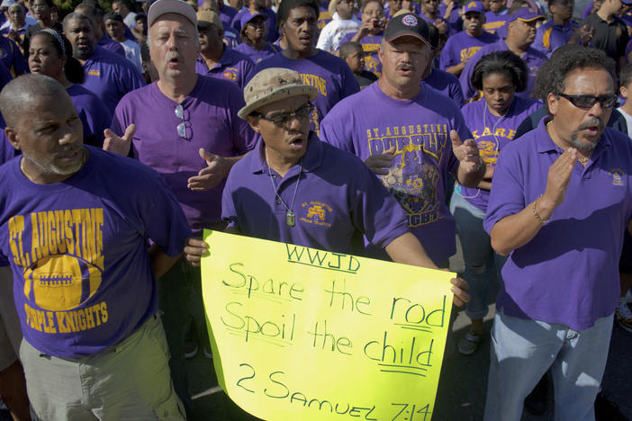 In this March 26, 2011 file photo, supporters of St. Augustine High School, including Byron Bernard, class of 1980, center, with "Spare the Rod, Spoil the Child" poster, demand the right of self-governance, including a corporal punishment policy, march and cheer in front of the Archdiocese of New Orleans at Notre Dame Seminary.