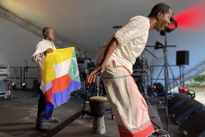 Global musicians can run into daunting red tape when it comes to obtaining a visa to perform at festivals. Soubi Attoumane (left) and M'madi Djibaba (right) of the band Comorian from Comoros had to fly to another country to apply for a U.K. visa to come to Peter Gabriel's WOMAD festival. Above: They unfurl the Comorian flag to a standing ovation at the concert on July 31.