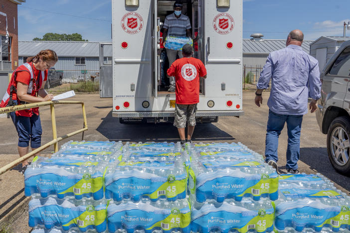 Michelle Hartfield, a public information officer for the Salvation Army, takes notes while Booker Ellis, Chris Bonham and Walter Houston unload water donated by the Salvation Army to the Mississippi Industries for the Blind on Thursday.