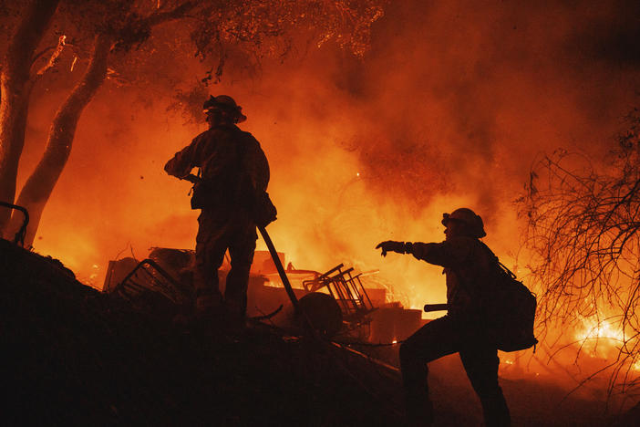 Firefighters coordinate efforts at a burning property while battling the Fairview Fire on Monday, near Hemet, Calif.