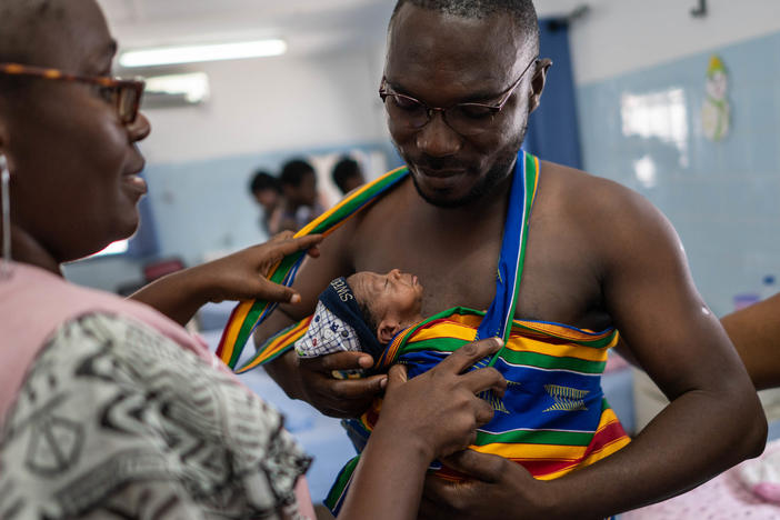 New father Yappe Pako gets help with his kangaroo care carrier from midwife Marie-JosÃ©e Miezan. His newborn son is named Ambo Crisostome. They're in the kangaroo care ward at the University Hospital Medical Center at Treichville in the Ivory Coast. A new program teaches the technique to moms â and dads. It's especially beneficial for preterm and low birthweight babies.