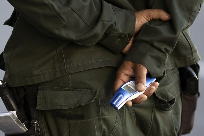 A municipal police officer holds a no-touch forehead thermometer at a checkpoint amid increased restrictions on residents' movements in an effort to curb the spread of the new coronavirus in Niteroi, Brazil, Monday, May 11, 2020.