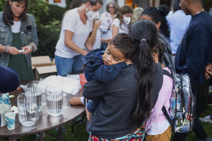 A woman, who is part of a group of migrants that had just arrived, holds a child as they are fed outside St. Andrews Episcopal Church on Wednesday in Edgartown, Mass., on Martha's Vineyard. Florida Gov. Ron DeSantis flew two planes of migrants to Martha's Vineyard on Wednesday.
