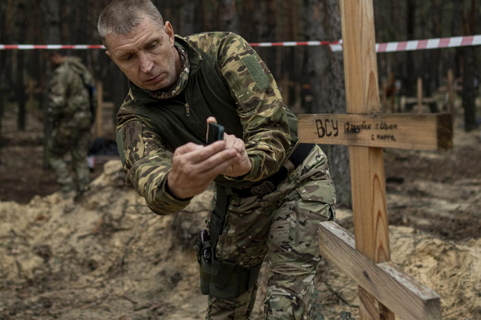 Oleg Kotenko, the commissioner for issues of missing persons under special circumstances, uses his smartphone to film the grave a Ukrainian soldier in the recently retaken area of Izium, Ukraine, Sept. 15, 2022.