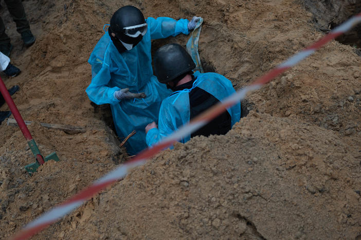 Ukrainian investigators exhume bodies from a mass grave site in Izium on Friday.