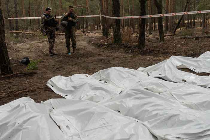 Ukrainian soldiers stand over bags containing the remains of exhumed bodies at a mass grave site in Izium, Ukraine.
