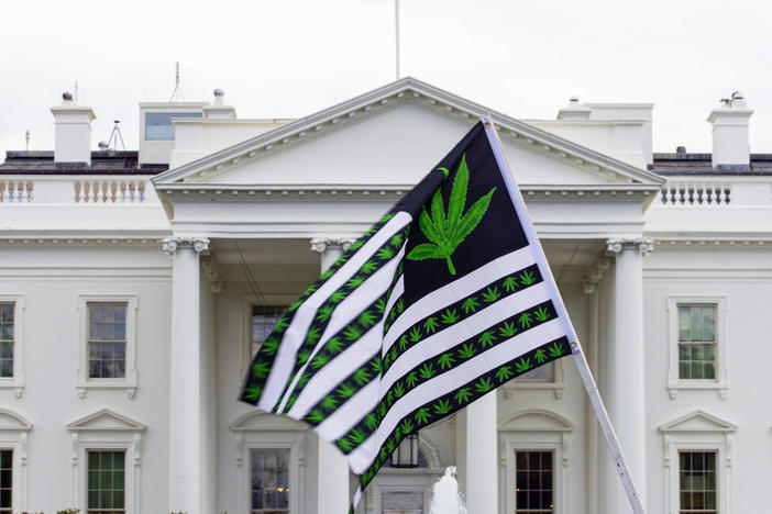 A demonstrator waves a marijuana-themed flag in front on the White House. President Biden is pardoning thousands of Americans convicted of "simple possession" of marijuana under federal law.