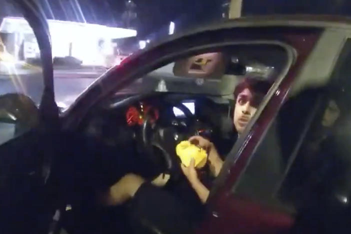 In this image taken from Sunday, Oct. 2, 2022, police body camera video and released by the San Antonio Police Department, Erik Cantu looks toward San Antonio Police Officer James Brennand while holding a hamburger in a fast food restaurant parking lot.