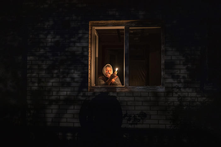 A resident looks out the window holding a candle for light inside her house during a power outage, in Borodyanka, Kyiv region, Ukraine, Thursday. Airstrikes cut power and water supplies to hundreds of thousands of Ukrainians on Tuesday, part of what the country's president called an expanding Russian campaign to drive the nation into the cold and dark.