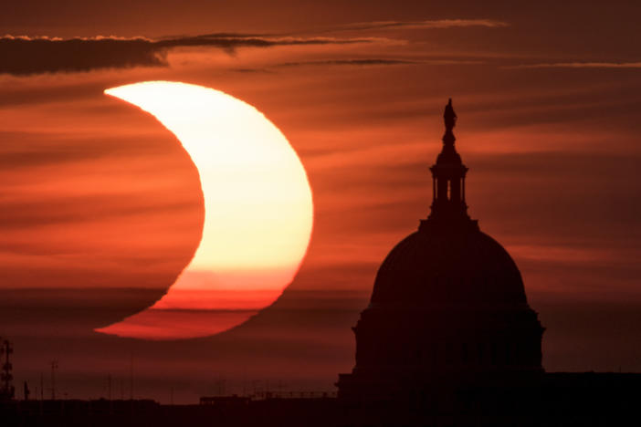 In this photo provided by NASA, a partial solar eclipse is seen as the sun rises to the left of the U.S. Capitol in Washington, Thursday, June 10, 2021, as seen from Arlington, Va.