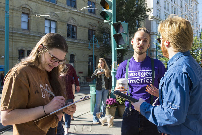 Matthew Grover (center) of NextGen America talks with young voters Kate Browning (left) and Jack Borg as they sign a pledge promising to vote near the Milwaukee Public Market on Saturday.