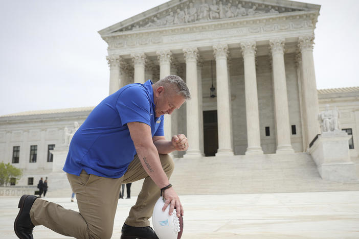 Joseph Kennedy, seen here taking a knee in front of the U.S. Supreme Court last spring, will return to coach at Bremerton High School. His practice of praying on the field sparked a court case over accommodating religious expression in public schools.