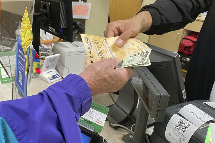 From behind the lottery counter at a Pick 'n Save store in Madison, Wis., Djuan Davis hands Powerball tickets to Arpad Jakab, a retired utility worker who said it's his first time buying them.