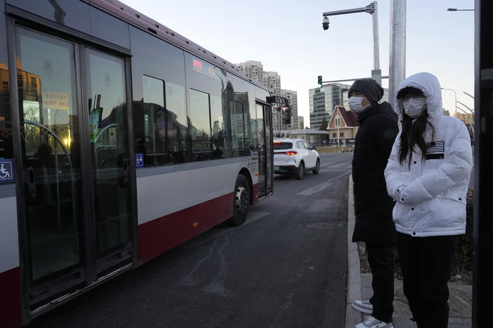 Residents wearing masks wait at a public bus stop in Beijing on Saturday. Chinese authorities announced a further easing of COVID-19 curbs with major cities such as Shenzhen and Beijing no longer requiring negative tests to take public transport.