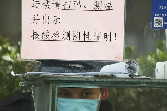 A security guard keeps watch inside a booth outside an office building in Beijing, Monday, Dec. 12, 2022.