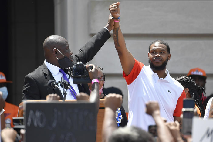 Attorney Benjamin Crump (left) holds up the hand of Kenneth Walker during a rally on the steps of the Kentucky State Capitol in Frankfort, Ky., on June 25, 2020. Walker, the boyfriend of Breonna Taylor who fired a shot at police as they burst through Taylor's door the night she was killed, has settled two lawsuits against the city of Louisville, his attorneys said.