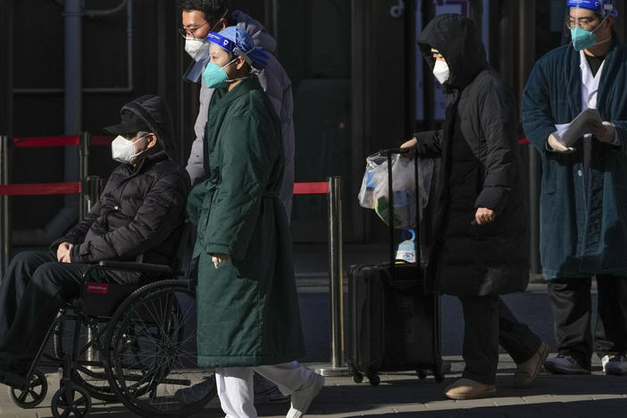 Medical workers in protective gear escort an elderly patient on a wheelchair followed by family members as they leave a fever clinic at a hospital in Beijing on Monday, Dec. 19, 2022.