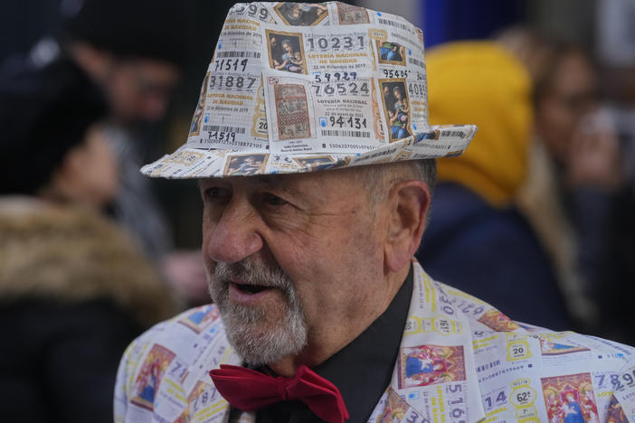 A man with a suit and hat decorated in printed lottery tickets stands outside the famous Doña Manolita lottery ticket shop in downtown Madrid, Spain, Wednesday, Dec. 21, 2022.